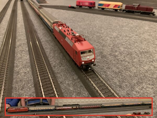 Eine Rote E-Lok vor einem Personenzug aus Wagen in Ozeanblau/Beige und Orientrot/Beige.